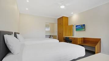 A hotel room with a large bed, a desk, a chair, a wooden wardrobe, and a TV mounted on the wall.