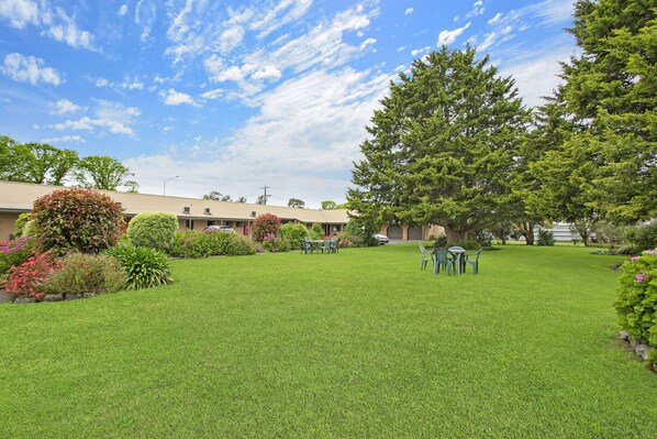 A well-maintained garden with a lawn, a dining area with outdoor furniture, and a building with a beige exterior.