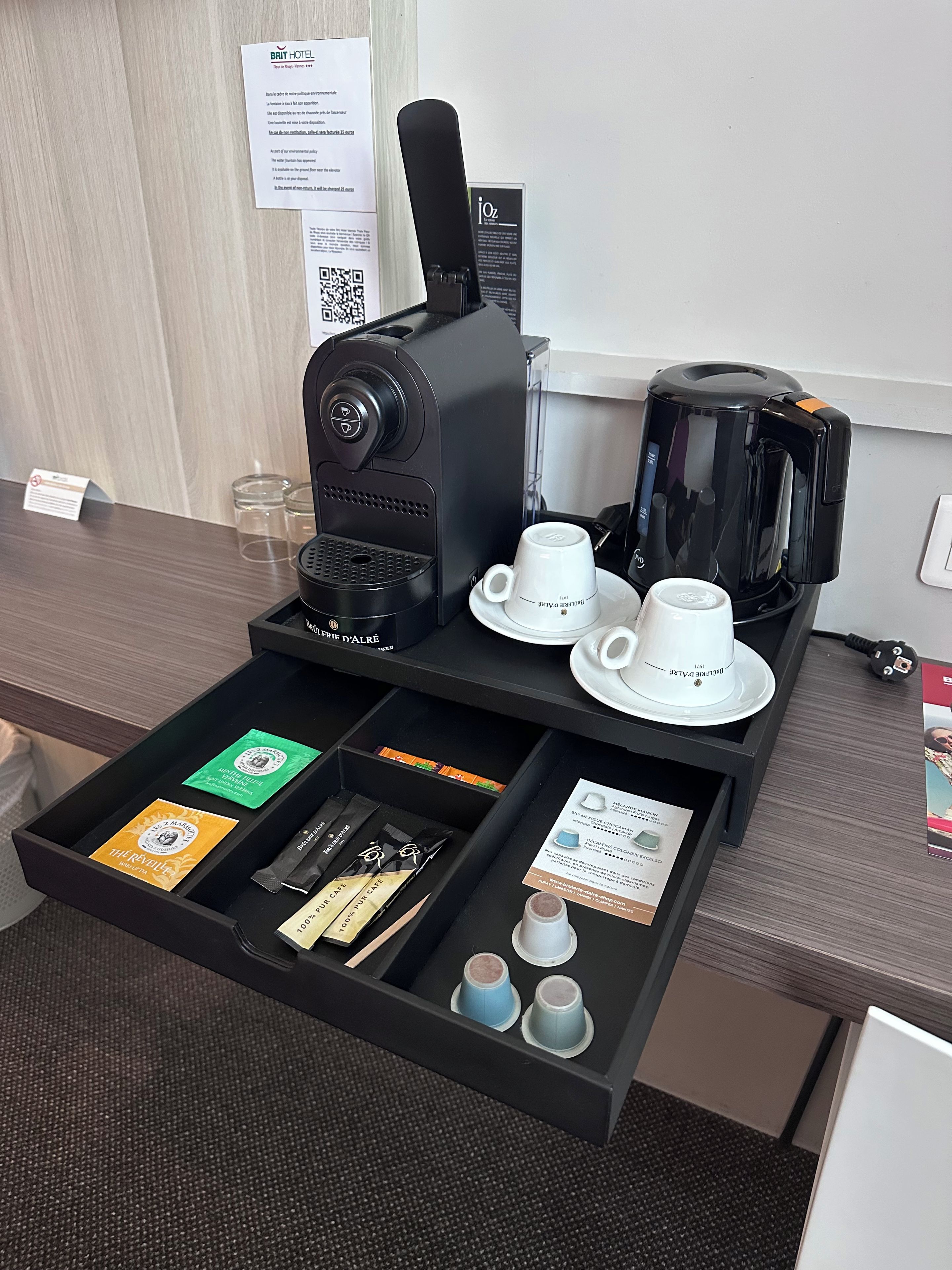 A coffee station with a coffee machine, cups, and a tray with coffee pods and a menu.