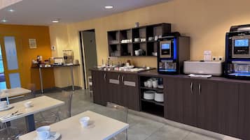 Un café moderno con mesas, sillas, una máquina de café y una estación de autoservicio para bebidas.