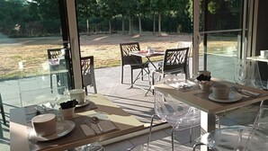 A dining area with glass tables and chairs, a view of a grassy field, and a clear sky. - Brit Hotel Vannes-Theix (Theix-Noyalo)