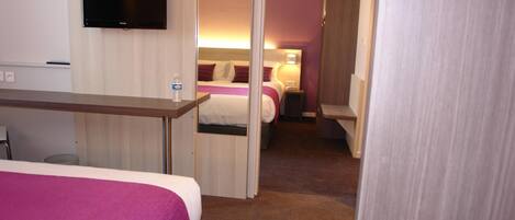 Habitación de hotel con cama, escritorio, televisión y baño visible a través de una puerta abierta.