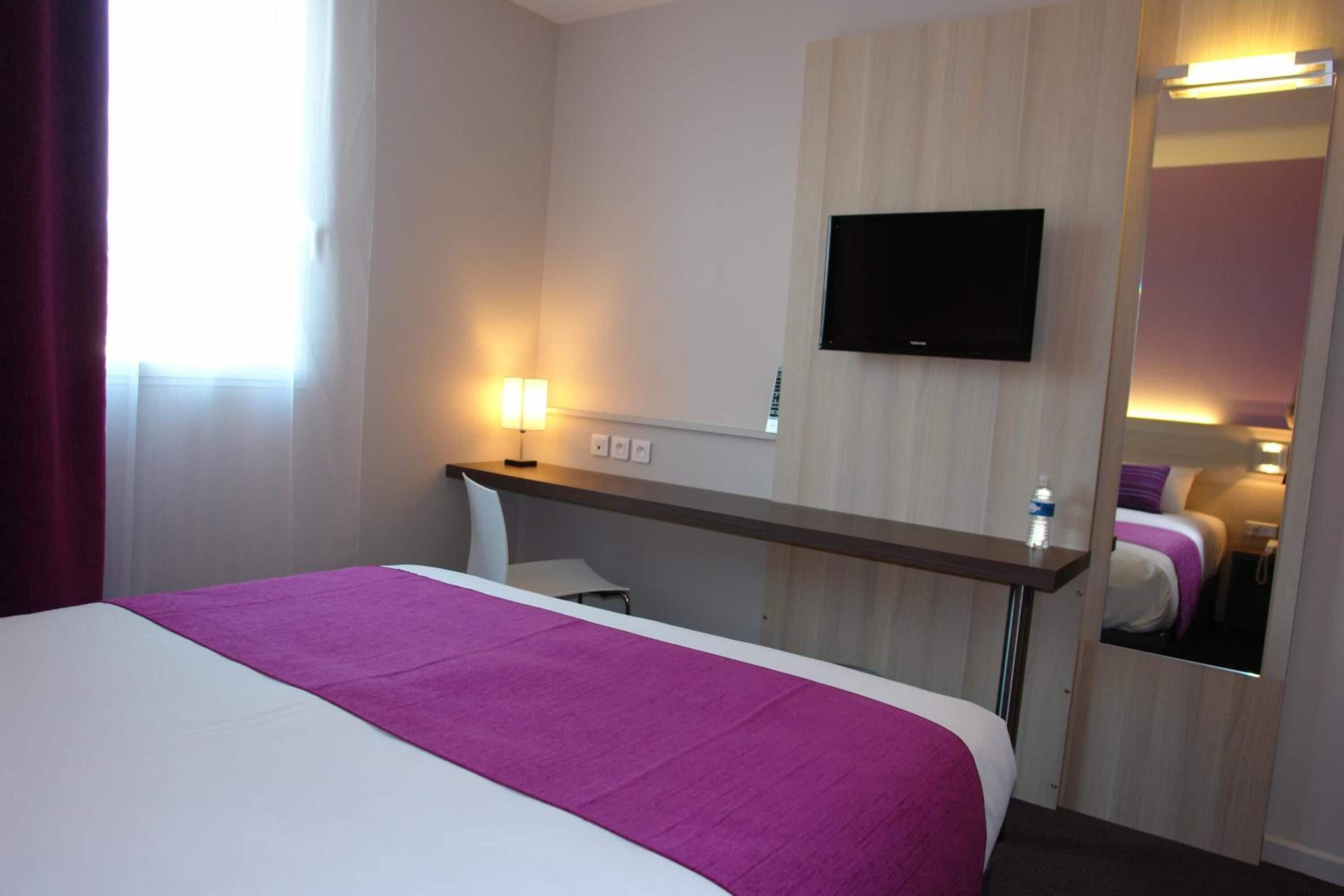 Une chambre d’hôtel avec un lit, un bureau, une télévision et un miroir.