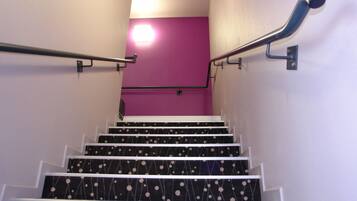 Una escalera con peldaños negros adornados con lunares blancos, barandas blancas y una pared morada en la parte superior.