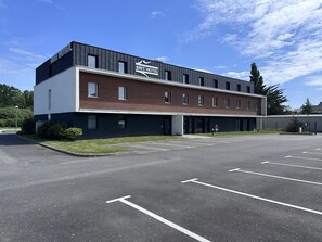 A modern hotel building with a flat roof, multiple windows, and a parking lot in front.
