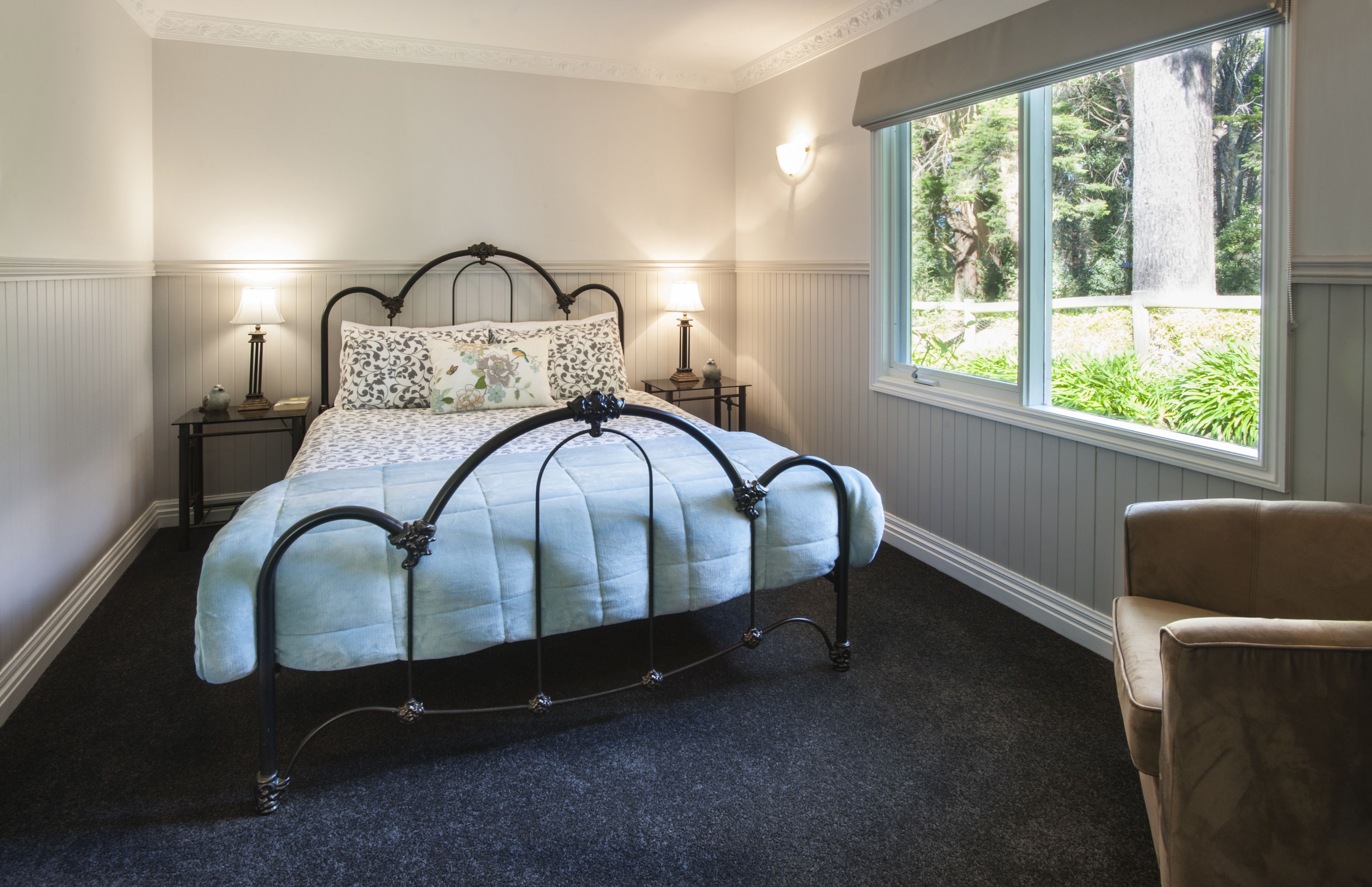 A bedroom with a bed, two bedside tables, a window with a view of greenery, and a chair.