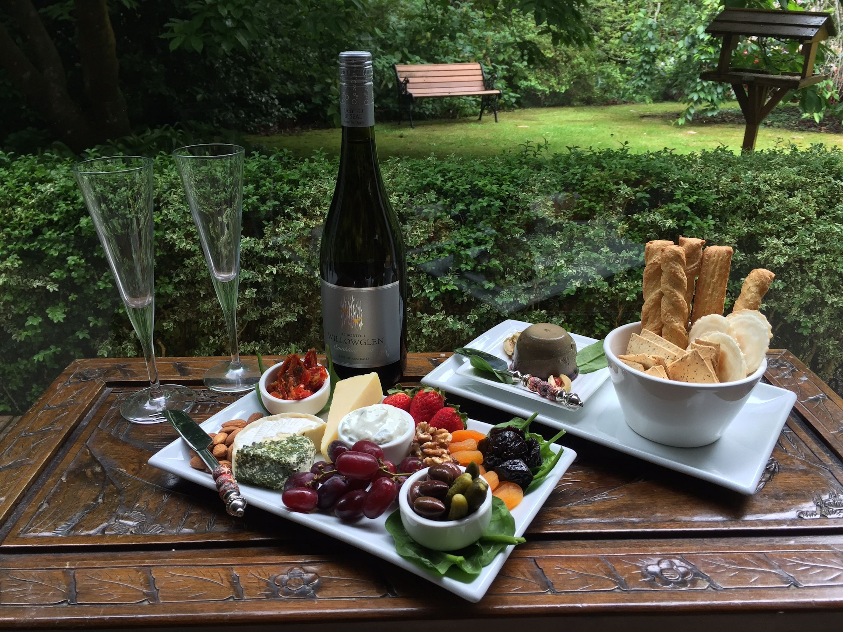 A table with a bottle of wine, glasses, and a variety of cheeses, fruits, and nuts.