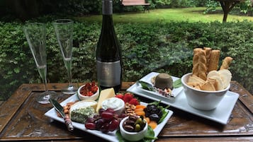 A table with a bottle of wine, glasses, and a variety of cheeses, fruits, and nuts.