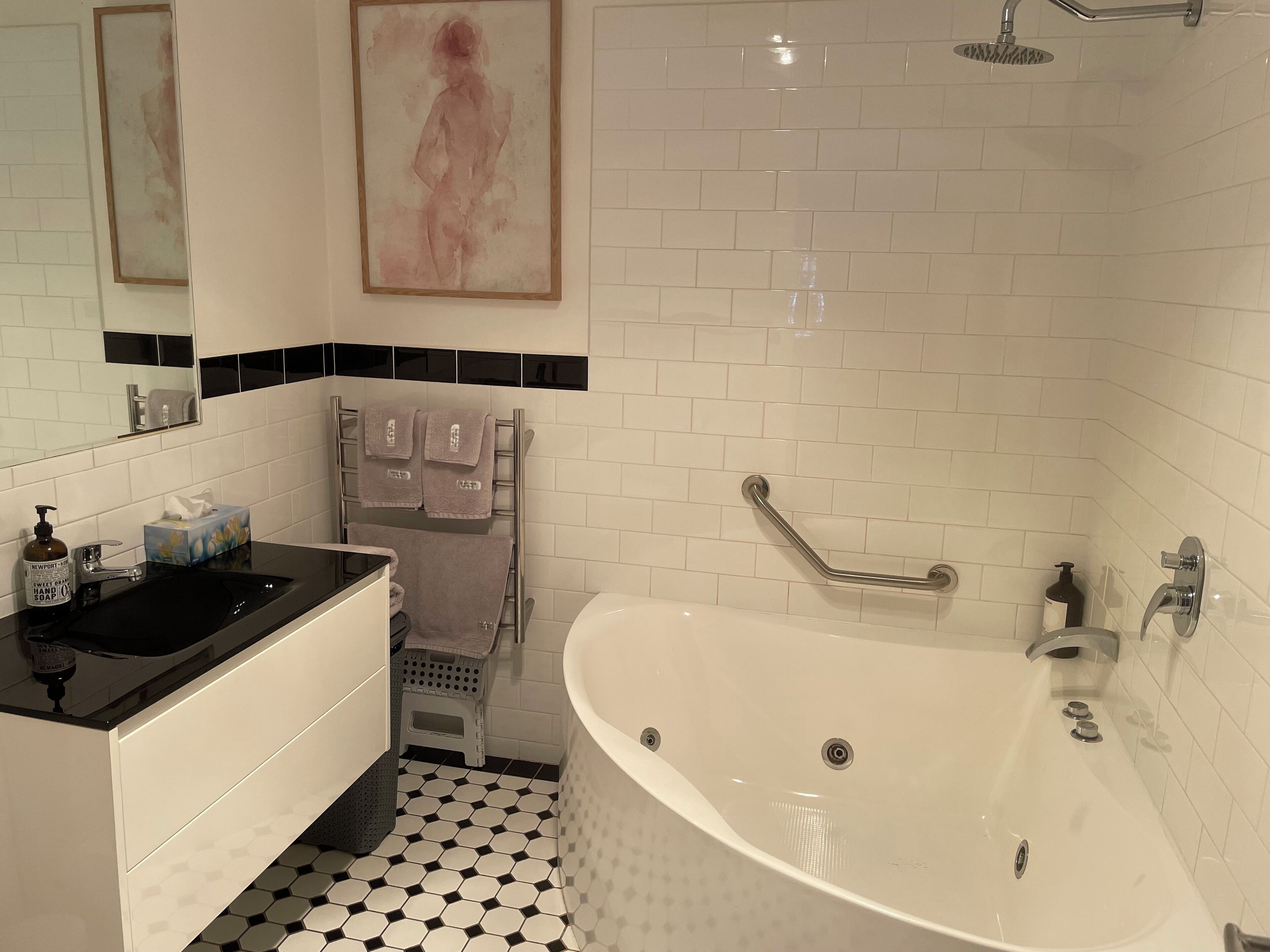 A bathroom with a white bathtub, a black countertop sink, a hand soap dispenser, and a small stool.