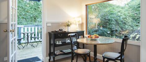 Un coin repas comprenant une table ronde, deux chaises, une petite table d’appoint avec une lampe, et une vue sur la verdure à l’extérieur.
