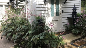 A white house with a green door, a bird feeder, and pink flowers in the garden. - Clarendon Cottages (Sassafras)