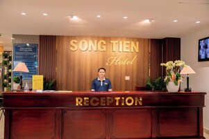 Una mesa de recepción en el Hotel SONG TIEN con un fondo de madera y un cartel que indica la zona de recepción.