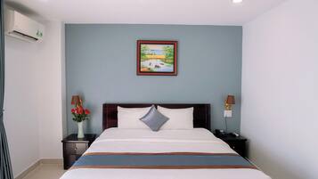 A hotel room with a bed, a nightstand with a lamp, a picture on the wall, and an air conditioning unit.