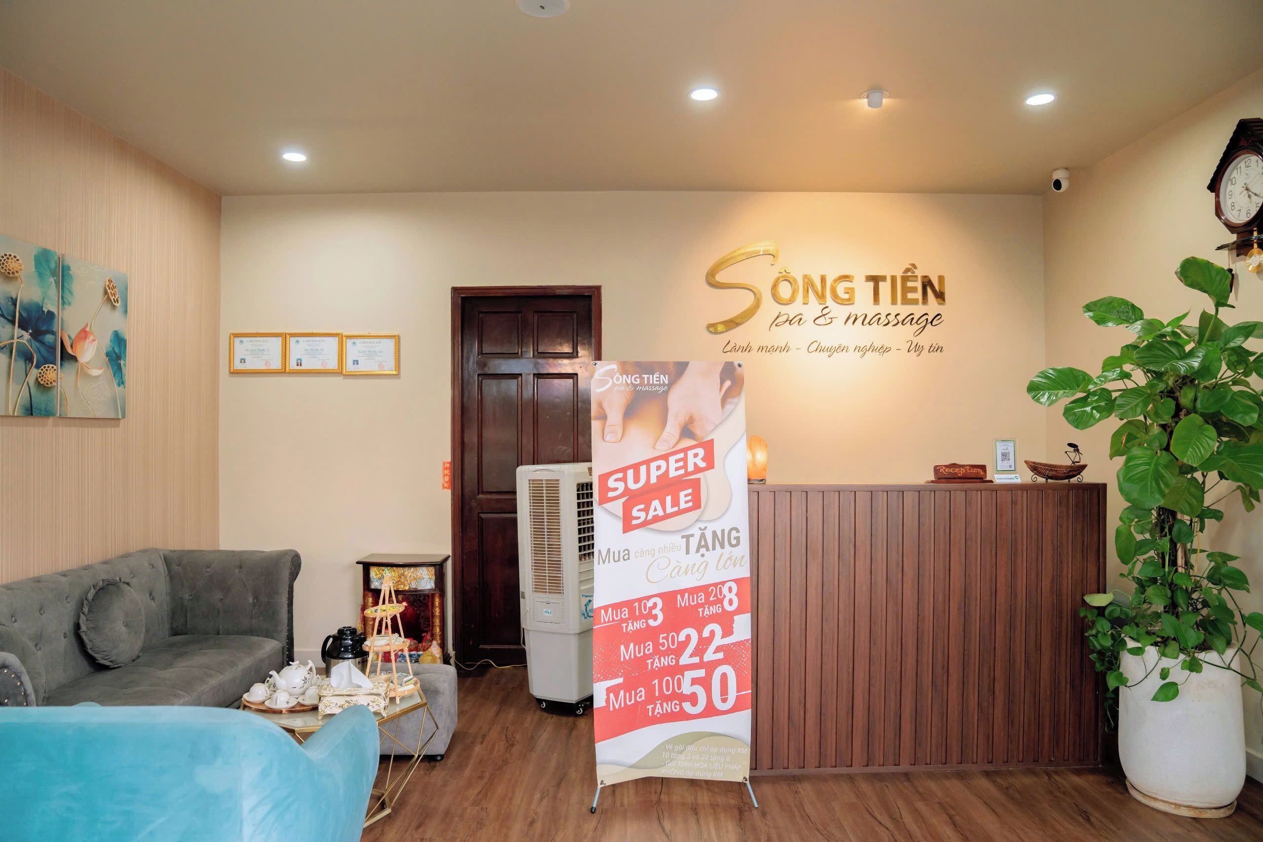 A reception area with a wooden reception desk, a blue sofa, a grey sofa, a wall with a massage service sign, and a 'Super Sale' poster.