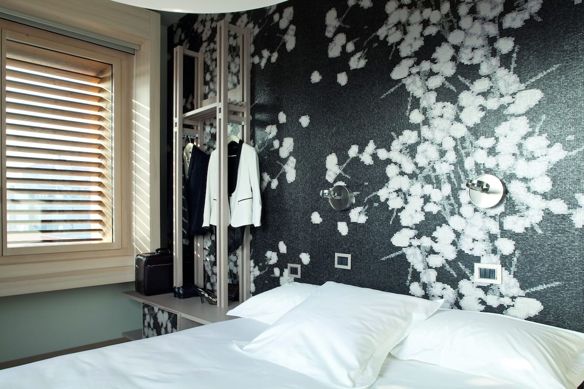 A hotel room with a bed, a wardrobe, and a window with blinds.