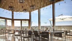 A spacious restaurant with high ceilings, hanging light fixtures, and large windows offering a view of the sky. - NU Hotel (Milan)
