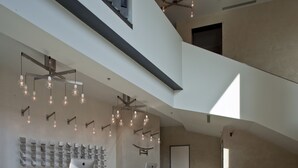 A modern reception area with a high ceiling, exposed ductwork, and a series of pendant lights. - NU Hotel (Milan)