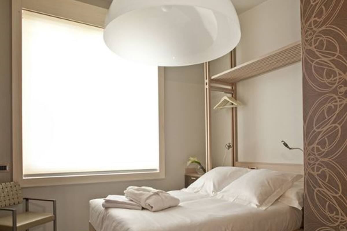 A bedroom with a bed, a chair, a hanging light fixture, and a window.