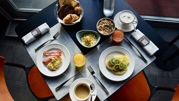 Une table de petit-déjeuner avec des croissants, des œufs brouillés, des tranches de kiwi, un verre de jus d’orange, une tasse de café et un verre de jus de fruits.