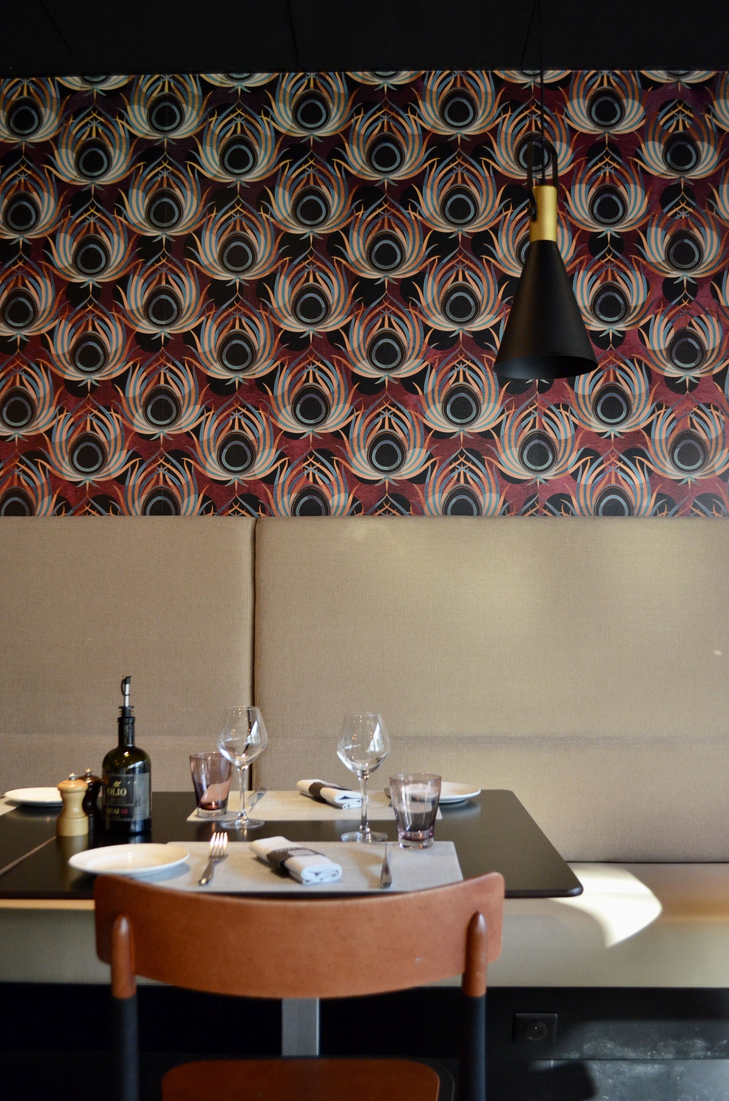 Comedor con papel tapiz estampado, una mesa dispuesta con una botella, vasos y cubiertos, y una lámpara colgante.