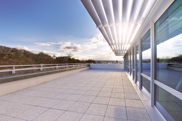 Una terraza en la azotea con diseño moderno, que presenta una barandilla de cristal y vistas a la ciudad.