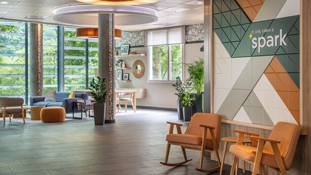 A modern lobby with seating areas, a large window with a view of greenery, and a wall with a geometric pattern and the text "It only takes a spark". - Spark by Hilton Lyon Ouest (Lyon)