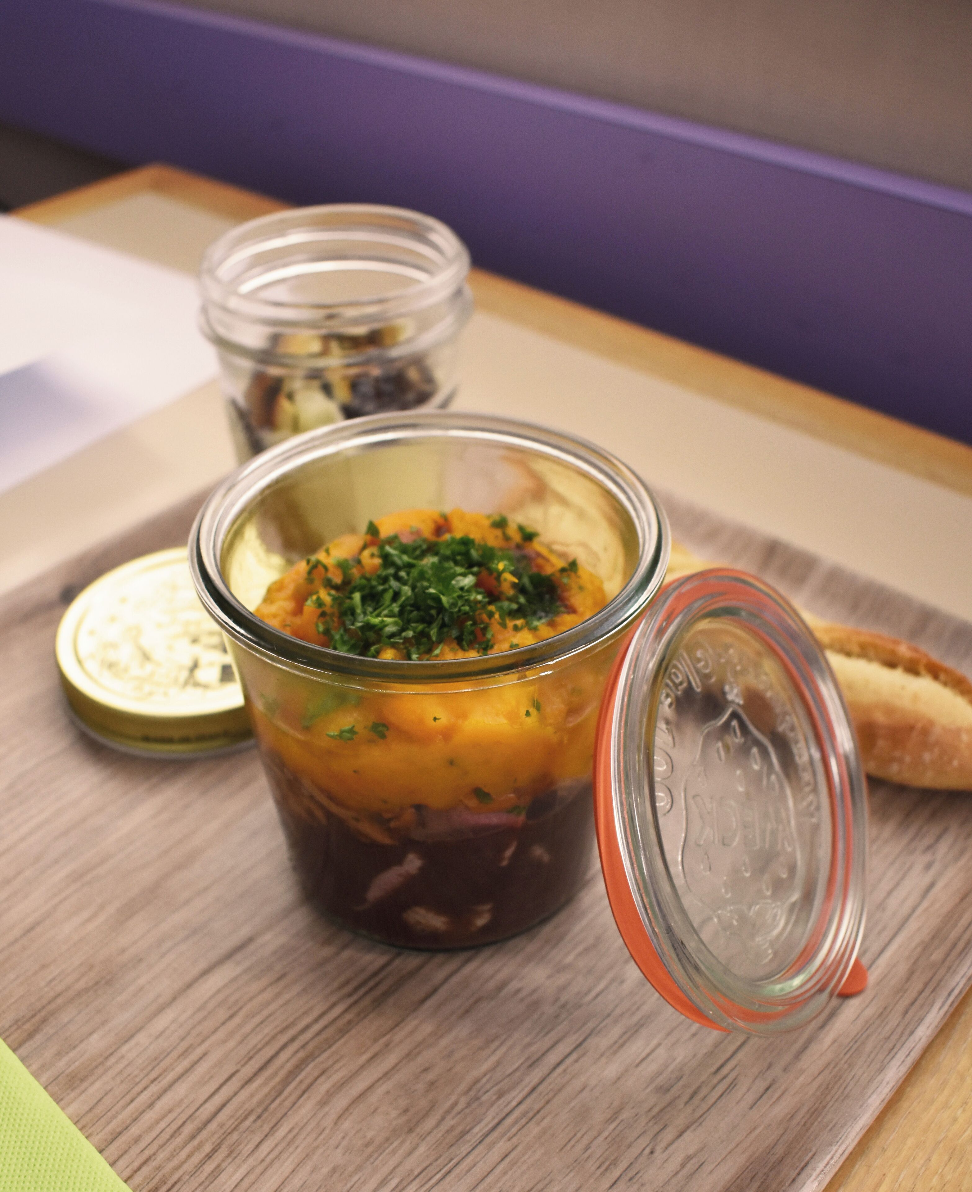 A jar of food with a lid on a wooden tray.