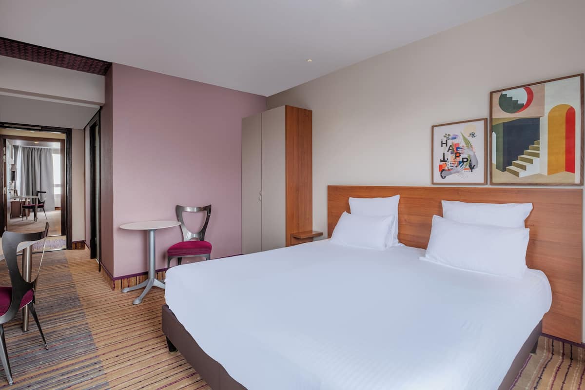 Ein Hotelzimmer mit einem großen Bett, einem Schreibtisch mit Stuhl, einem kleinen Tisch und Kunstwerken an den Wänden.