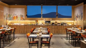 A modern dining area with multiple tables and chairs, a counter with kitchen appliances, and large windows with a view of the mountains. - Spark by Hilton Lyon Ouest (Lyon)