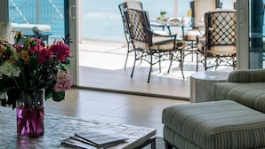 A room with a view of the ocean, a ceiling fan, a table with a vase of flowers, and a seating area with chairs. - Caribbean Club Luxury Condo Hotel (Seven Mile Beach)