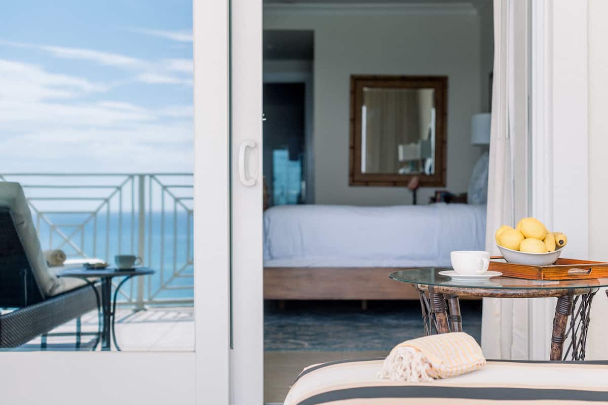 Habitación de hotel con balcón, una cama, una mesa con frutero y una silla.