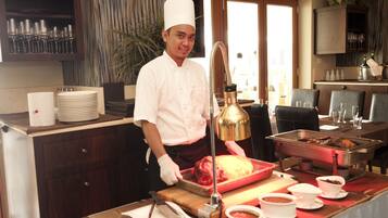 Un chef con uniforme blanco preparando comida en una cocina con mesas tipo buffet.
