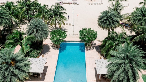 An aerial view of a resort with a swimming pool, palm trees, and a beach. - Caribbean Club Luxury Condo Hotel (Seven Mile Beach)