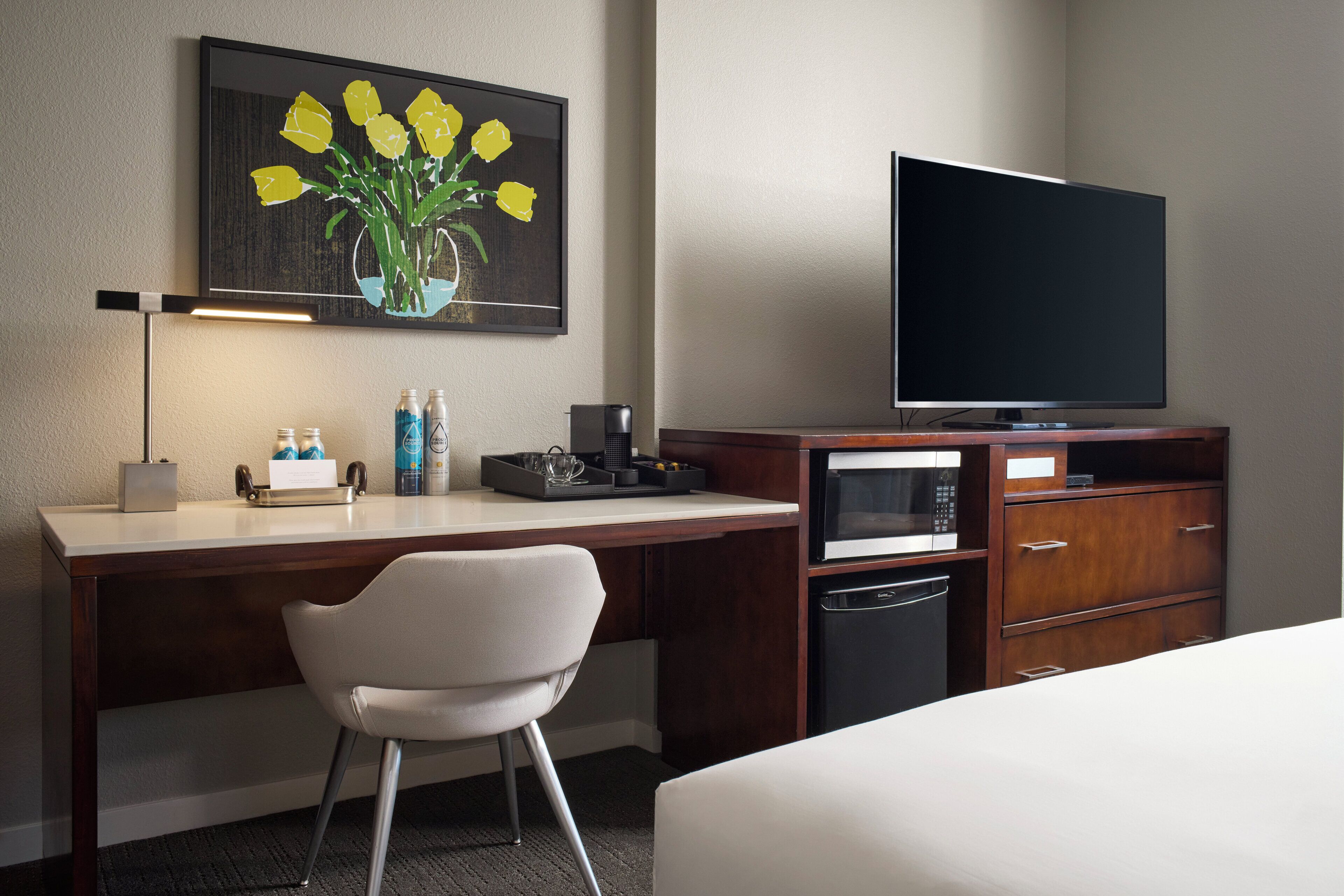 A hotel room with a bed, a desk with a chair, a television, a microwave, and a small cabinet.