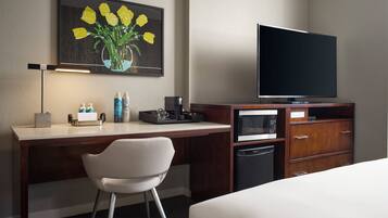 A hotel room with a bed, a desk with a chair, a television, a microwave, and a small cabinet.