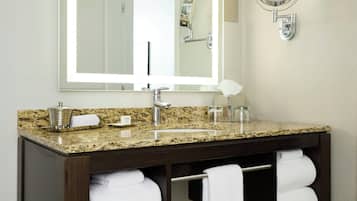 A bathroom with a granite countertop, a large mirror, a round vanity mirror, and two towels hanging on a rack.