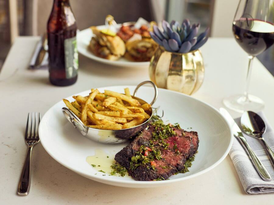 A dining table with a plate of steak and fries, a bottle, and a glass of red wine.