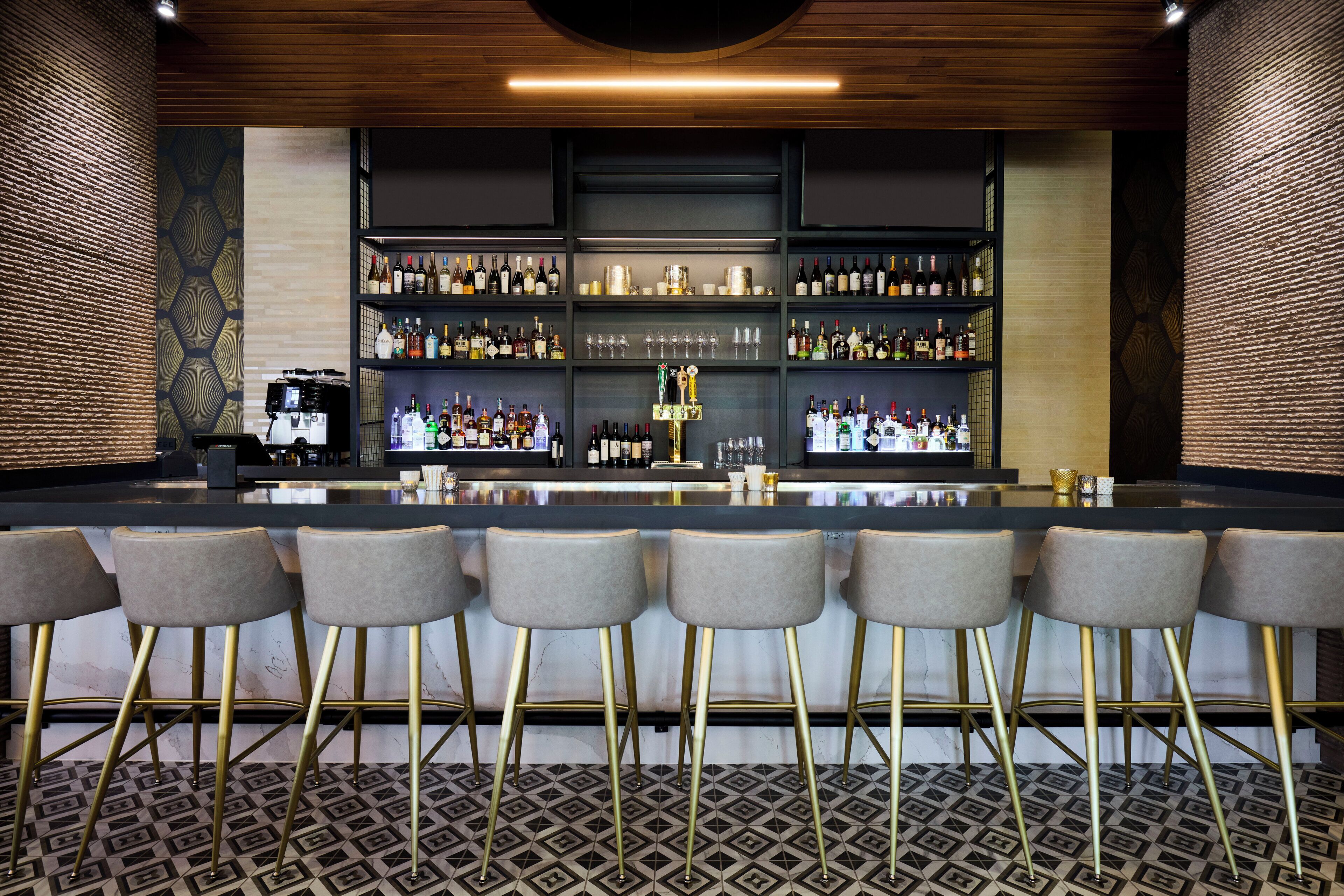 A bar area with a long counter, multiple shelves of bottles, and bar stools.
