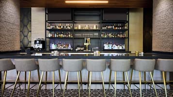 A bar area with a long counter, multiple shelves of bottles, and bar stools.