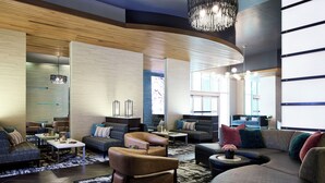 A modern hotel lobby with a curved wooden ceiling, a chandelier, sofas, armchairs, and a coffee table.