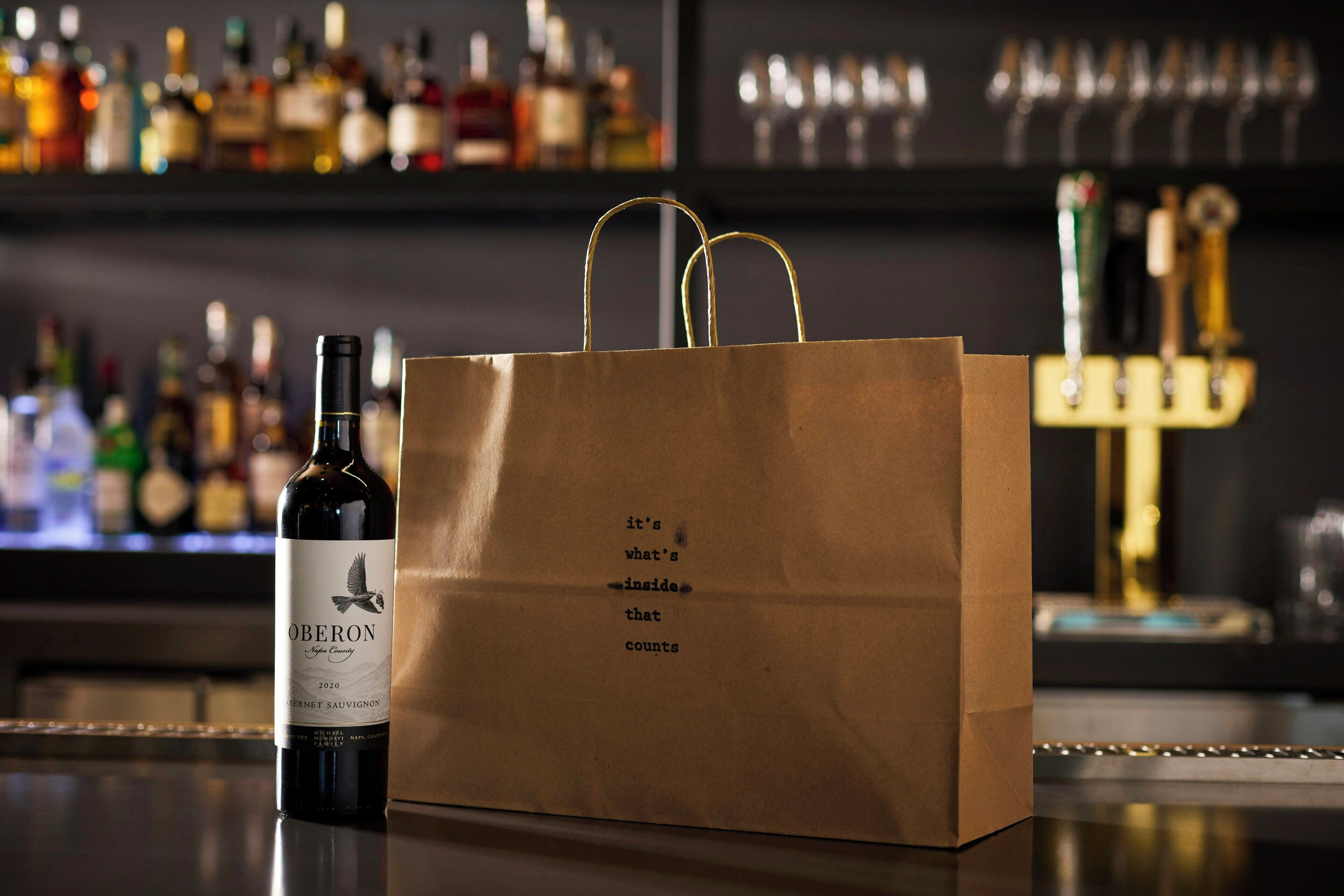 A bottle of wine and a brown paper bag with text on a bar counter.