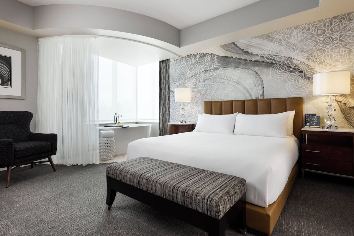 Una habitación de hotel con una cama grande, un banco, un escritorio y una silla.