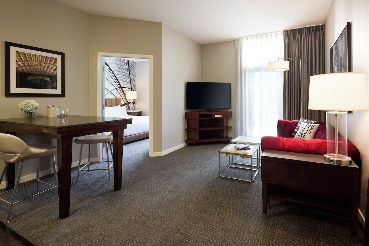 Una habitación de hotel con comedor, un sofá rojo, televisor y lámpara.