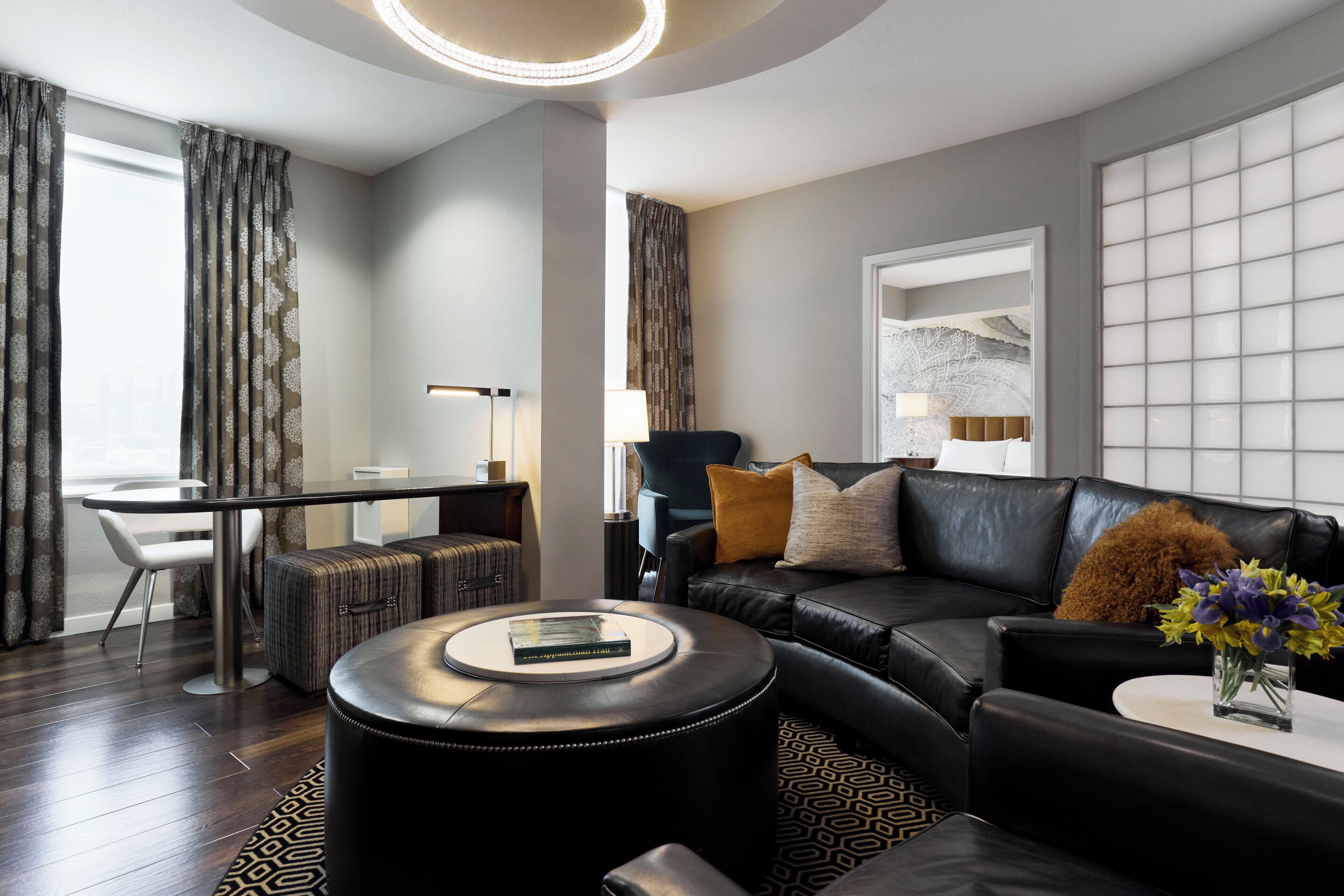 A modern living room with a black leather sofa, a round coffee table, and a dining area with a white table and chairs.