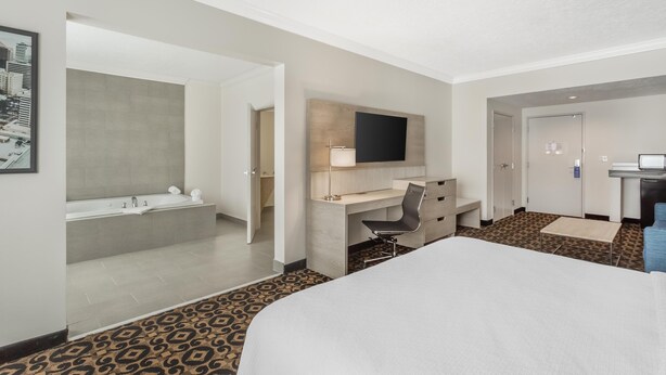 A hotel room with a large bed, a desk with a chair, a flat-screen TV, a bathroom with a bathtub, and a patterned carpet. - Best Western Plus Airport Inn & Suites (Salt Lake City)