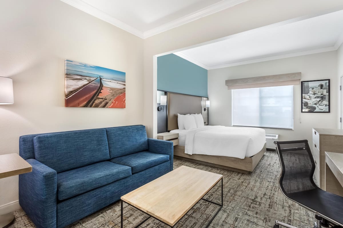 Une chambre d’hôtel avec un canapé bleu, un lit, un bureau et une table basse.