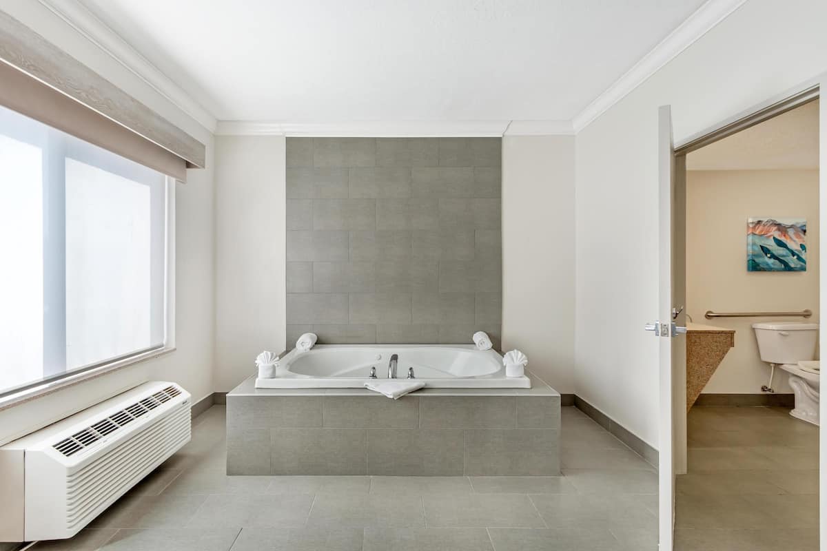 Une salle de bain moderne avec une grande baignoire, une fenêtre et un appareil de climatisation visible.