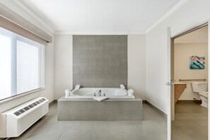 A modern bathroom with a large bathtub, a window, and a visible air conditioning unit.