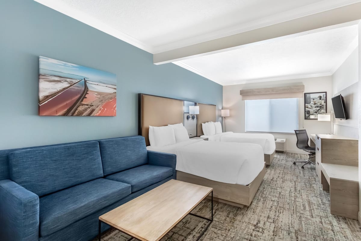 Une chambre d’hôtel avec un canapé bleu, deux lits, un bureau et une grande fenêtre.