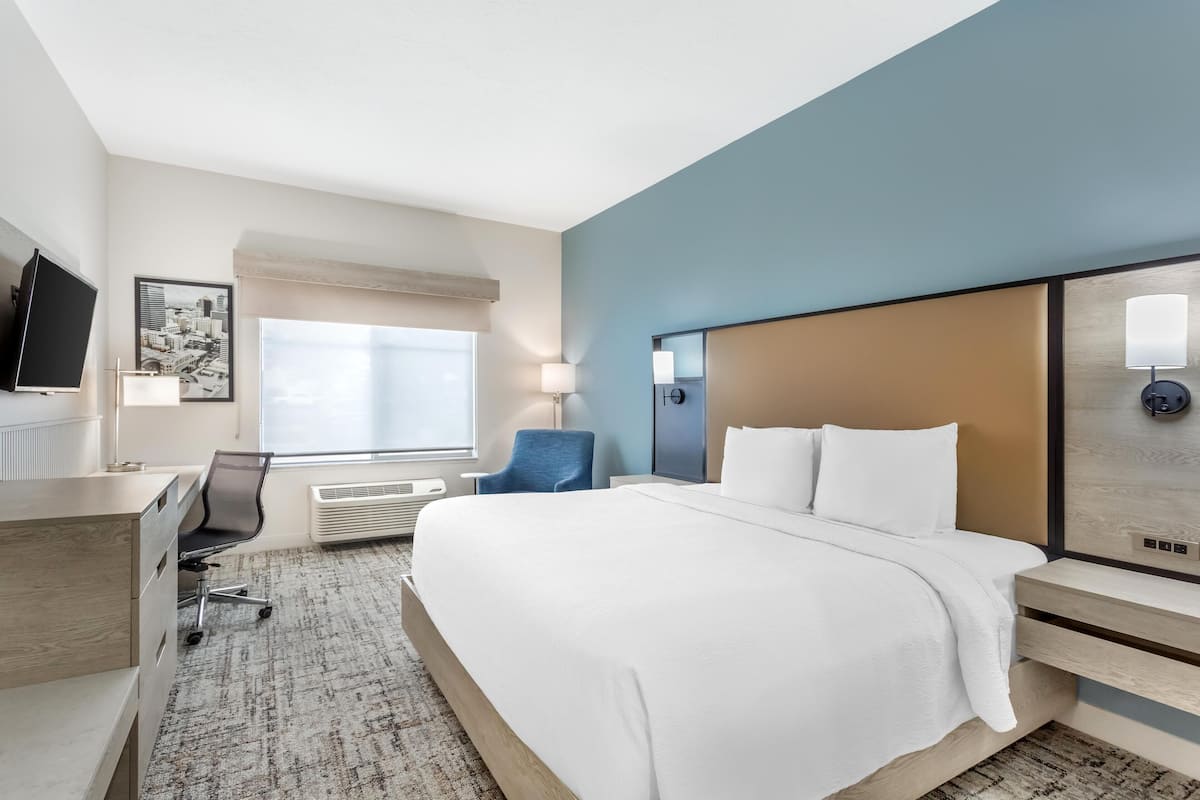 Une chambre d’hôtel avec un lit, un bureau, une chaise, une télévision et une fenêtre.